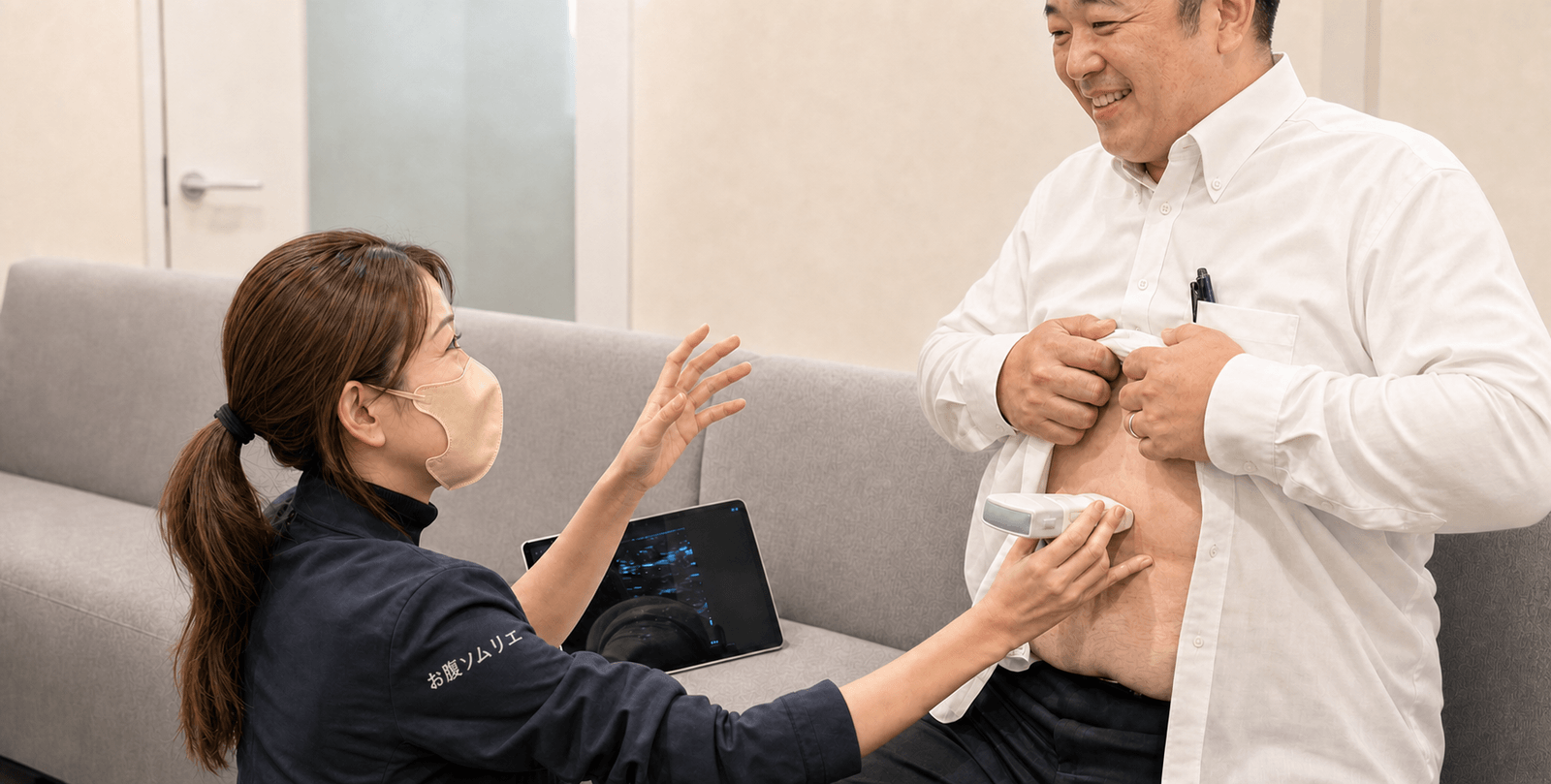 健康測定会での測定の様子。お腹ソムリエのスタッフが超音波プローブをお腹に当て、タブレットに映る内臓脂肪の画像を見ながら参加者に説明する